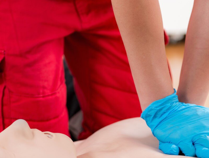 Erste Hilfe Kurs - Ersthelfer drückt mit beiden Händen auf den Brustkorb einer Wiederbelebungspuppe